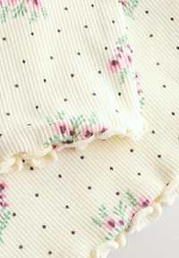Tejido crema acanalado con pequeños puntos marrones y grupos de flores rosas con hojas verdes, con bordes rizados y ondulados.