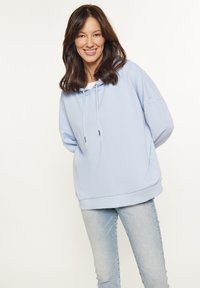 Felpa azzurra con cappuccio e cordino, vestibilità ampia e maniche lunghe. Abbinata a jeans in denim chiaro. Tessuto morbido, design casual.