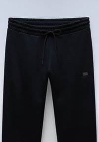 Schwarze Jogginghosen mit elastischem Bund und Kordelzug. Verfügt über ein kleines Markenlogo in einer dunkleren Farbnuance. Glatte, lässige Stofftextur.