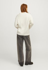 Maglione di colore crema con colletto a scialle, abbinato a pantaloni a gamba larga in corduroy grigi con orlo arrotolato e stivaletti neri chunky.