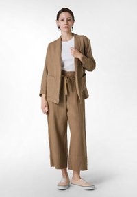 Linne tvådelat set i ljusbrun, med en löst sittande jacka med fickor och avslappnade vida byxor, som matchas med beige sneakers.