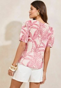 Roze bloes met bloemenprint en pofmouwen, gemaakt van lichte stof, met een tropisch bladerenpatroon en een ronde halslijn. Draag het met witte shorts.