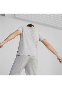 Camiseta de algodón gris con mangas cortas, corte relajado y etiqueta en la parte inferior, combinada con pantalones de chándal grises. Diseño sencillo, sin patrones.