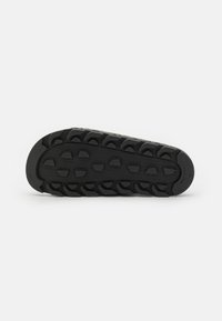 Semelle de chaussure de sport noire avec des motifs de profondeur pour l'adhérence, dotée d'une surface en caoutchouc texturé et d'une forme contournée pour le confort.