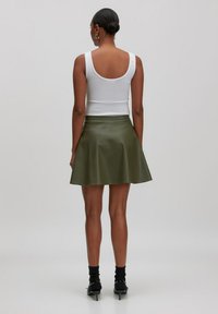 Un haut sans manches blanc associé à une jupe évasée en simili cuir olive. Des bottines et des chaussettes complètent la tenue. Texture lisse, design simple.