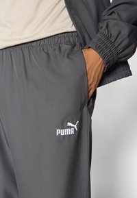 Pantaloni sportivi grigi realizzati in tessuto liscio, con vita elasticizzata e logo Puma bianco sul lato sinistro. Dettagli con tasche.