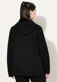 Felpa nera con cappuccio realizzata in tessuto testurizzato, con orlo e maniche a coste, dalla vestibilità comoda e fessure laterali per facilitare il movimento.