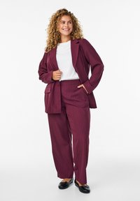 Bordeaux gestreifter Anzug mit einem entspannten Blazer und einer Hose, kombiniert mit einem weißen T-Shirt und schwarzen Ballerinas, die eine glatte Stofftextur zeigen.