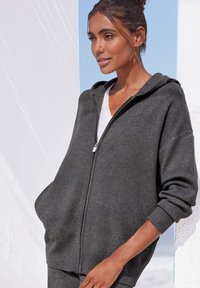 Charcoalgraue Zip-Hoodie aus weichem Material mit lässiger Passform, langen Ärmeln und Kapuze, ausgestattet mit seitlichen Taschen und gerippten Bündchen.