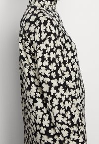 Zwarte blouse met een bloemenpatroon in het wit, hoge kraag, lange mouwen en een relaxte pasvorm. De stof lijkt glad met een subtiele glans.