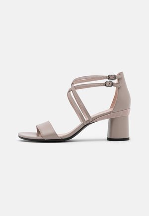 Beige dame sandal med åben tå, to justerbare ankremme og blokhæl, vist i sideprofil på en neutral baggrund.