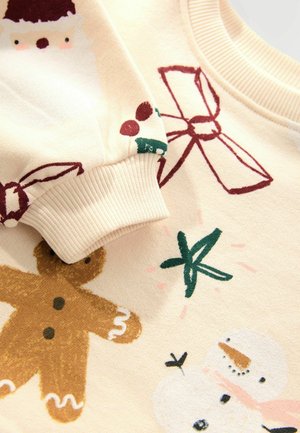 Svetlo krémový mikina s vianočnými potlačami Santa Clausa, perníkových mužov a snehuliakov. Rukávy s rebrovaným okrajom dodávajú textúru a detail.