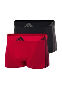 Dvě sady pánských boxerek Adidas, jedny v sytě červené barvě s černým logem a bočními pruhy, a jedny v jednobarevné černé barvě se šedým logem a pruhy.