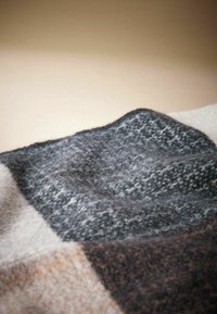 Pilkas ir juodas raštuotas vilnonis antklodė su minkšta, pūkuota tekstūra, pasižyminti geometrinių formų ir subtilių spalvų variacijų mišiniu.