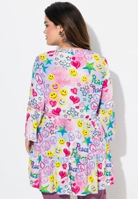 Multikleurige jurk met een speelse print van glimlachen, harten, sterren en vredessymbolen; lange mouwen met ruches.