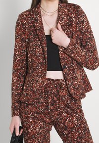 Leopardmönstrad kavaj i nyanser av röd, brun och svart, med skräddarsydd passform, enkel knäppning och mjuk tygtextur.
