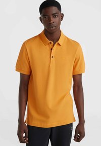 Camisa polo naranja de manga corta, con cuello y tapeta de tres botones, y un pequeño logo. Textura suave y corte relajado.