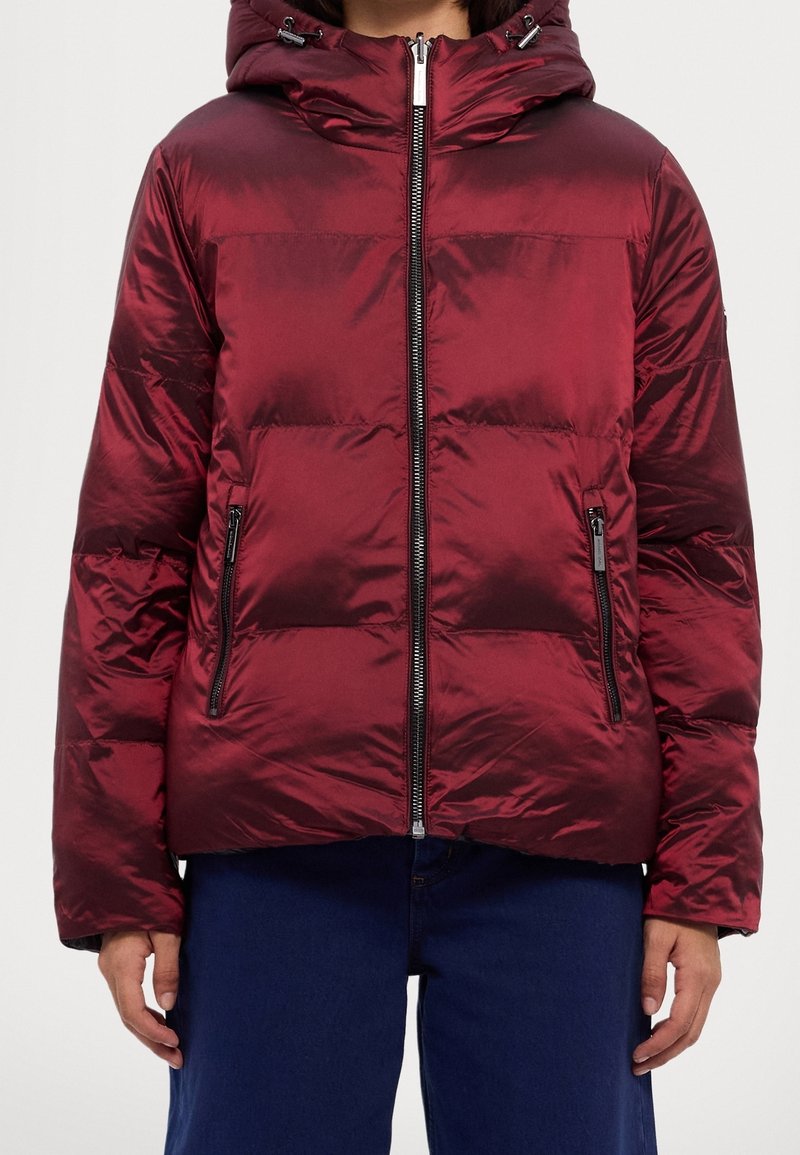 Veste rouge matelassée à finition brillante, dotée d'une capuche, d'une fermeture éclair avant et de deux poches latérales zippées. Structurée avec des coutures horizontales.