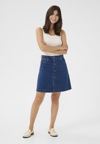 Jeans A-linje kjol i mörkblå med knappstängning fram, fem fickor och en sömdetalj, ihopparad med en vit ärmlös topp.