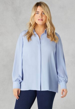 Blusa azzurra chiara con maniche lunghe a pieghe, chiusura con bottoni e vestibilità comoda. Realizzata in tessuto morbido con una texture liscia.