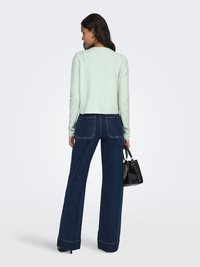 Hellmintgrüner Strickpullover mit langen Ärmeln, kombiniert mit hochtaillierter, dunkelblauer Jeans mit weitem Bein, die einen groben Saum und Gesäßtaschen aufweist.