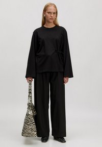 Zwarte lange mouw top met een strikdetail, gecombineerd met losse zwarte broek en een zebra-gepatenteerde tas. Soepele stof en een relaxte pasvorm.