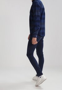 Námořnické modré pruhované tričko s dlouhým rukávem vyrobené z lehké tkaniny, spárované s tmavě modrými skinny džíny a bílými teniskami. Jednoduché knoflíkové detaily.