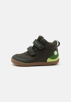 Dunkelgrüner Kinderschuh mit zwei Klettverschlüssen, hellbrauner Sohle und Froschgesicht-Design an der Ferse.