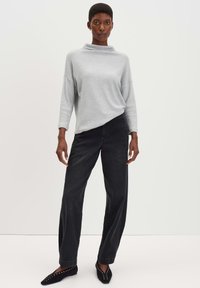 Maglione grigio chiaro a collo alto con maniche a trequarti, abbinato a jeans neri a gamba dritta e scarpe nere basse con dettagli borchiati.