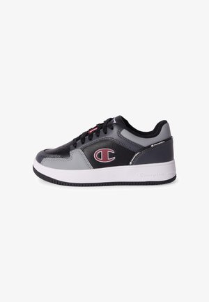Zwart-grijze lage sneaker met witte zool, zwarte veters en een rood-wit Champion-logo aan de zijkant.