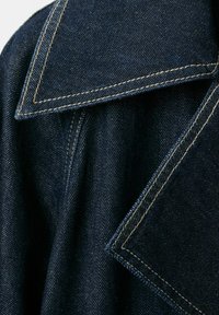 Tela de mezclilla azul oscuro con costuras dobles detalladas que forman un cuello amplio y una solapa.