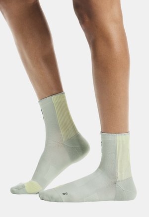 Calcetines verde claro con textura acanalada, detalles en amarillo pálido contrastante y puntera reforzada. Longitud hasta la mitad de la pantorrilla con detalle de logotipo.