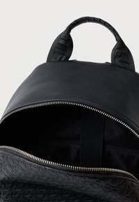 Mochila preta com um topo suave e uma seção inferior texturizada. Apresenta um fecho com zíper, alças de tecido e um design minimalista.