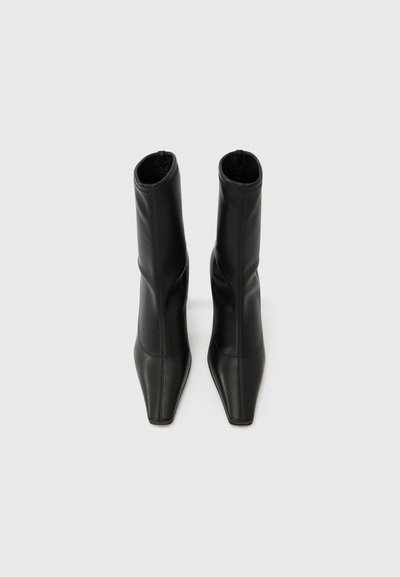 Melni potīšu zābaki no gludas ādas ar pieguļošu dizainu, smailu purngalu un smalkām šuvēm. Kvadrātveida papēži.