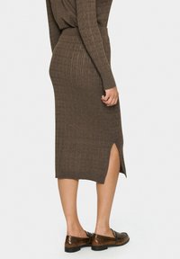Jupe midi en tricot marron côtelé avec une fente sur le côté et une taille élastique, associée à des mocassins marron. Tissu texturé avec une silhouette ajustée.