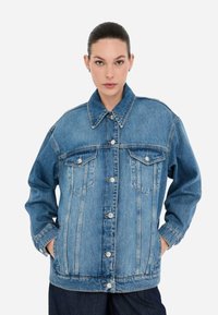 Giacca in denim blu con chiusura a bottoni, ampio colletto, due tasche sul petto e vestibilità rilassata, con un leggero sbiadimento e dettagli di cucitura.