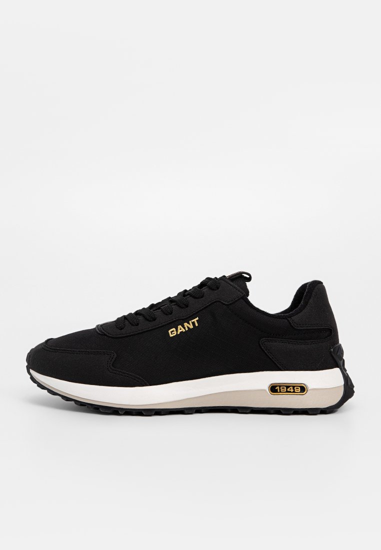 Zapatillas de tela negra con un logo dorado, cuello acolchado y una mediasuela blanca con detalle del año. Suela de goma texturizada para un buen agarre.
