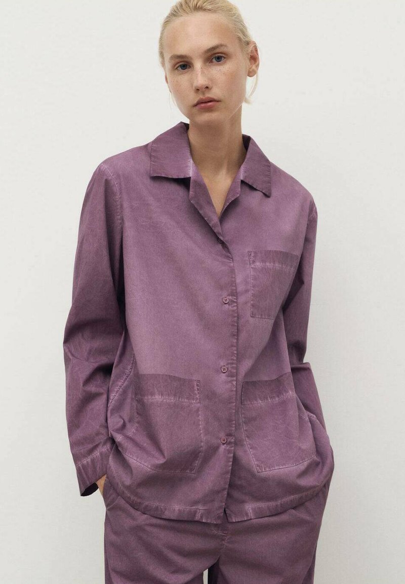 Purple button-up shirt with a collar, featuring two front pockets and a relaxed fit. Smooth texture with a slightly crinkled appearance.