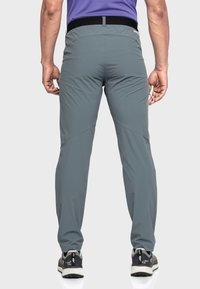 Graue Sporthosen mit einer strukturierten Oberfläche, ausgestattet mit einem schwarzen elastischen Bund und einem schmal zulaufenden Bein, kombiniert mit schwarzen und grauen Sneakern.