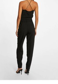 Top negro sin mangas con textura brillante, combinado con pantalones negros de tiro alto que cuentan con un cinturón y bolsillos, llevados con sandalias de tacón negro.