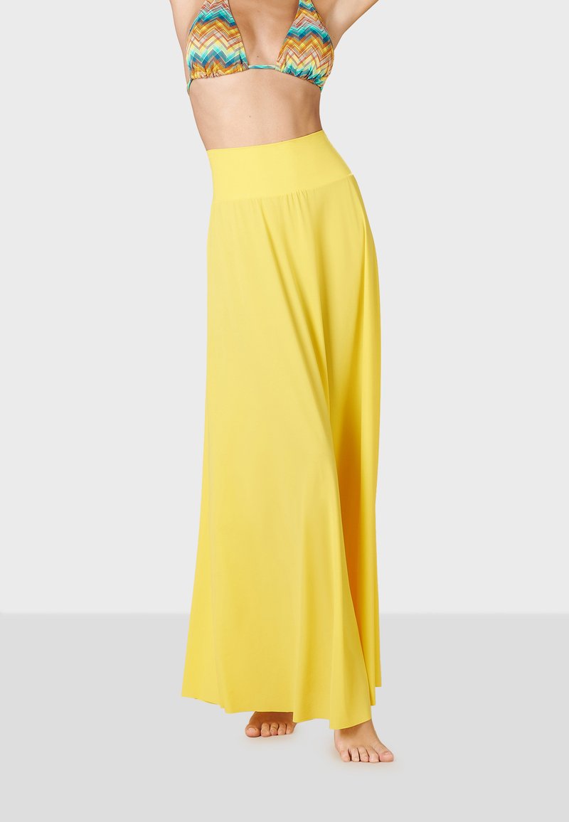 Falda maxi amarilla con una amplia cinturilla elástica, tela fluida, textura suave y una silueta amplia, llevada sobre un sujetador de bikini estampado.