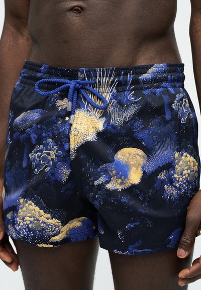 Ανδρικός κορμός και άνω πόδια που φοράνε σκουρό μπλε μαγιό με μοτίβα κίτρινου και μπλε κοραλλιογενούς υφάλου και μπλε κορδόνι δεμένο στη μέση.