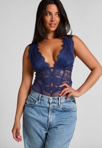 Marineblauw kanten bodysuit met een diepe V-hals, doorschijnende gaaspanelen, bloemenpatronen en korte mouwen, gecombineerd met lichtblauwe high-waisted jeans.