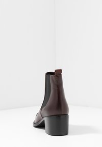 Bootie din piele maronie, cu toc bloc, panouri elastice laterale și sistem de prindere. Textură netedă și design aerodinamic.