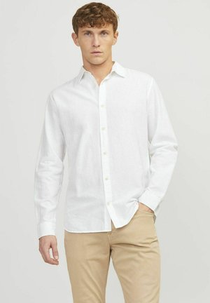 Camicia bianca a maniche lunghe realizzata in tessuto leggero con chiusura a bottoni e colletto classico, abbinata a pantaloni color khaki.