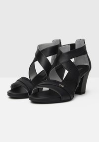 Sorte læder højhælede sandaler med krydsede stropper, åben tå og robust blokhæl. Har en subtil metallisk detalje på siden.