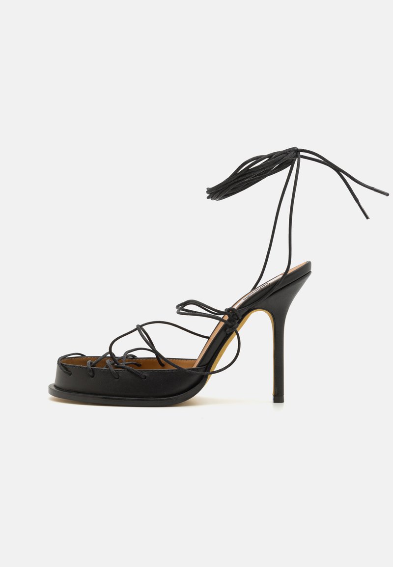 Sandalia negra de tacón alto con diseño de cordones, punta abierta y plataforma gruesa. Material de cuero suave con acentos minimalistas.