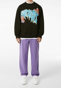 Svart sweatshirt med "FANTASY" grafik i blått och tecknade björnar. Matchas med lösa lila jeans och vita sneakers. Ren design.