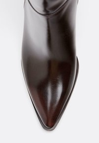 Brązowy skórzany botek do kostki z wąskim nosekiem, o gładkim wykończeniu i smukłym obcasie. Projekt charakteryzuje się minimalnym przeszyciem i elegancką sylwetką.