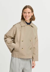 Veste beige à double boutonnage avec un large col, de grands boutons et une coupe décontractée, fabriquée en matériau léger. Dispose de poches latérales.